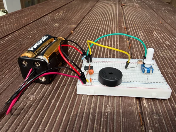 A breadboard circuit with a battery pack, buzzer and potentiometer on a wooden table